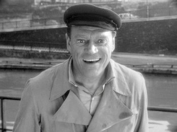 Movie still from “Cléo from 5 to 7” (1962), directed by Agnès Varda – A man wearing a hat and a trench coat; Close Up shot, High angle