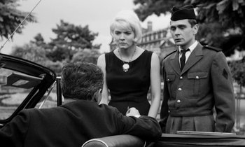 Movie still from “Cléo from 5 to 7” (1962), directed by Agnès Varda – A man and a woman standing next to each other in front of another man; Medium shot, Low angle