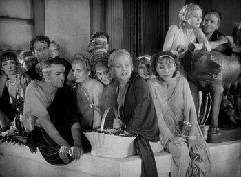 Movie still from “Cleopatra” (1934), directed by Cecil B. DeMille – A group of people that are sitting on a bench; Medium shot, High angle
