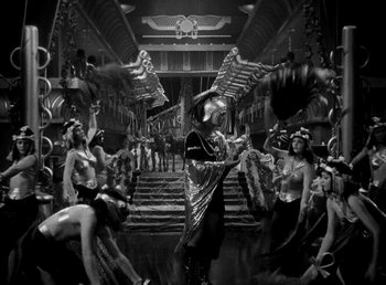 Movie still from “Cleopatra” (1934), directed by Cecil B. DeMille – A group of people standing in a room with a statue; Wide shot, High angle