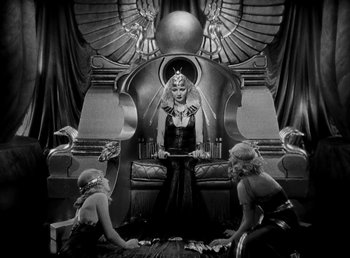 Movie still from “Cleopatra” (1934), directed by Cecil B. DeMille – A woman sitting on top of a throne in a room; Wide shot, High angle