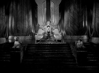 Movie still from “Cleopatra” (1934), directed by Cecil B. DeMille – A man sitting on top of a chair in front of an egyptian statue; Extreme Wide shot, High angle