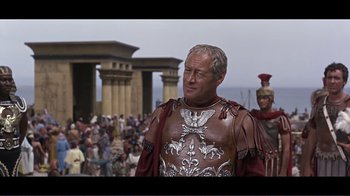 Movie still from “Cleopatra” (1963), directed by Rouben Mamoulian – A man in a roman soldier costume standing in front of a crowd of people; Medium shot, Over the shoulder angle