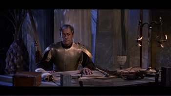 Movie still from “Cleopatra” (1963), directed by Rouben Mamoulian – A man sitting at a table wearing armor; Medium shot, High angle
