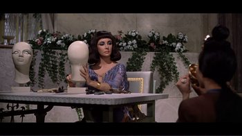 Movie still from “Cleopatra” (1963), directed by Rouben Mamoulian – A woman sitting at a table with a wig on her head; Medium shot, Over the shoulder angle