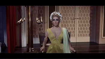 Movie still from “Cleopatra” (1963), directed by Rouben Mamoulian – A woman wearing a yellow dress and a crown; Medium shot, High angle