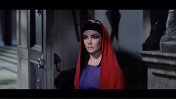 Movie still from “Cleopatra” (1963), directed by Rouben Mamoulian – A woman in a purple dress and a red head covering; Close Up shot, Over the shoulder angle