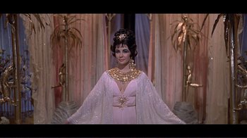 Movie still from “Cleopatra” (1963), directed by Rouben Mamoulian – A woman in a white dress standing in a room; Medium shot, Over the shoulder angle