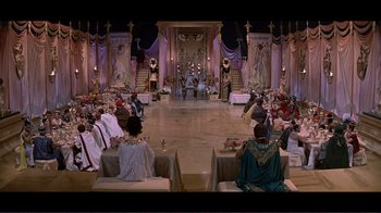 Movie still from “Cleopatra” (1963), directed by Rouben Mamoulian – A group of people sitting on chairs in front of a stage; Extreme Wide shot, High angle
