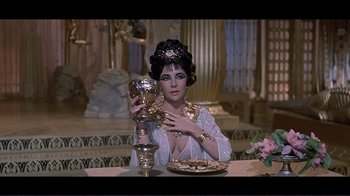 Movie still from “Cleopatra” (1963), directed by Rouben Mamoulian – A woman sitting at a dinner table holding a wine goblet; Medium shot, High angle