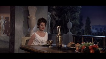 Movie still from “Cleopatra” (1963), directed by Rouben Mamoulian – A woman sitting at a table with a vase and a plate of food in front of her; Medium shot, High angle