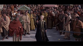 Movie still from “Cleopatra” (1963), directed by Rouben Mamoulian – An old man is holding an umbrella in front of a group of people; Wide shot, High angle