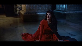 Movie still from “Cleopatra” (1963), directed by Rouben Mamoulian – A woman sitting on the ground wearing a red dress; Medium shot, High angle