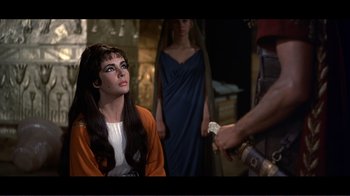 Movie still from “Cleopatra” (1963), directed by Rouben Mamoulian – A woman with long black hair sitting in front of two other women; Medium shot, Over the shoulder angle