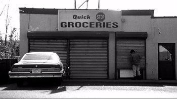 Movie still from “Clerks” (1994), directed by Kevin Smith – A black and white photo of a man standing in front of a grocery store; Wide shot, Low angle