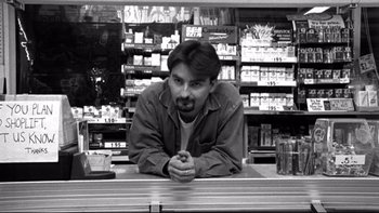 Movie still from “Clerks” (1994), directed by Kevin Smith – A black and white photo of a man sitting at a counter; Medium shot, Low angle