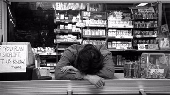 Movie still from “Clerks” (1994), directed by Kevin Smith – A man sitting at a counter in a store; Medium shot, Low angle