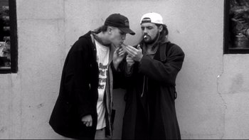 Movie still from “Clerks” (1994), directed by Kevin Smith – Two men standing next to each other and one of them is smoking a cigarette; Medium shot, High angle