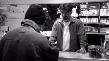 Movie still from “Clerks” (1994), directed by Kevin Smith – A man standing in front of a counter talking to another man; Medium shot, Over the shoulder angle