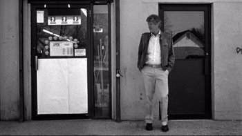 Movie still from “Clerks” (1994), directed by Kevin Smith – A black and white photo of a man standing in front of a store; Wide shot, Low angle