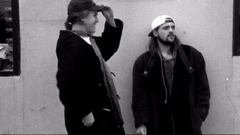 Movie still from “Clerks” (1994), directed by Kevin Smith – Two men standing next to each other on the side of a wall; Medium shot, Low angle