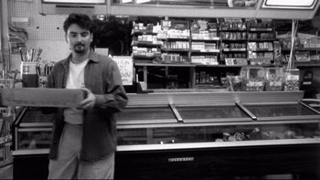 Movie still from “Clerks” (1994), directed by Kevin Smith – A black and white photo of a man standing in front of a display case; Medium shot, Low angle