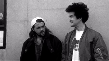 Movie still from “Clerks” (1994), directed by Kevin Smith – Two men standing next to each other in front of a wall; Medium shot, Low angle
