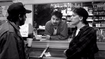 Movie still from “Clerks” (1994), directed by Kevin Smith – A man standing in front of two other men at a counter; Medium shot, Over the shoulder angle