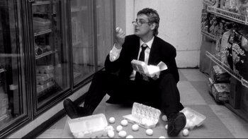 Movie still from “Clerks” (1994), directed by Kevin Smith – A black and white photo of a man sitting on the ground; Medium shot, Low angle