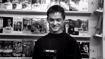 Movie still from “Clerks” (1994), directed by Kevin Smith – A man standing in front of a wall of books; Close Up shot, High angle