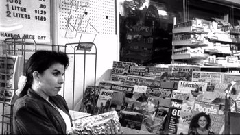 Movie still from “Clerks” (1994), directed by Kevin Smith – A black and white photo of a woman standing in front of a pile of magazines; Medium shot, Low angle
