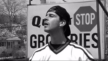 Movie still from “Clerks” (1994), directed by Kevin Smith – Black and white photograph of a young man in front of a sign; Close Up shot, Low angle