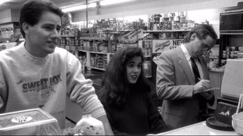 Movie still from “Clerks” (1994), directed by Kevin Smith – A woman sitting at a table with two men in the background; Medium shot, Over the shoulder angle