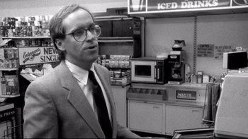 Movie still from “Clerks” (1994), directed by Kevin Smith – A black and white photo of a man standing in front of an oven; Medium shot, Over the shoulder angle