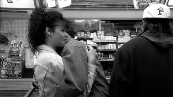 Movie still from “Clerks” (1994), directed by Kevin Smith – A woman sitting in a store next to a man; Medium shot, Over the shoulder angle