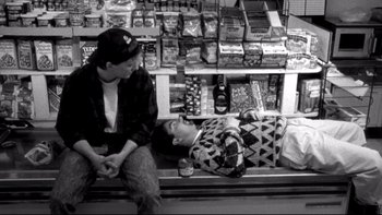 Movie still from “Clerks” (1994), directed by Kevin Smith – A couple of people sitting on top of a wooden bench; Wide shot, Overhead angle