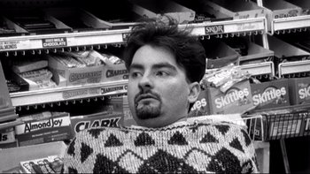 Movie still from “Clerks” (1994), directed by Kevin Smith – A black and white photo of a man in a sweater; Medium shot, High angle