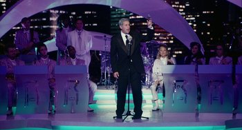 Movie still from “Click” (2006), directed by Frank Coraci – A man in a suit and tie holding a microphone; Wide shot, Over the shoulder angle