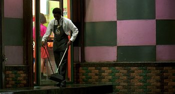 Movie still from “Clockers” (1995), directed by Spike Lee – A man in an apron holding a broom outside a building; Wide shot, High angle