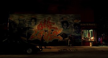 Movie still from “Clockers” (1995), directed by Spike Lee – A man standing in front of a wall covered in graffiti at night; Extreme Wide shot, Low angle