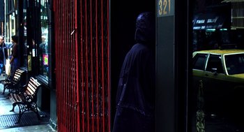 Movie still from “Clockers” (1995), directed by Spike Lee – A person in a hooded jacket standing in front of a red gate; Wide shot, Low angle