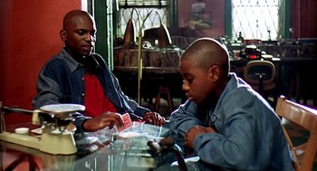 Movie still from “Clockers” (1995), directed by Spike Lee – A man and a boy sitting at a dining table; Medium shot, Over the shoulder angle