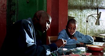 Movie still from “Clockers” (1995), directed by Spike Lee – A man and a boy sitting at a dining table; Medium shot, Low angle