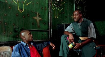 Movie still from “Clockers” (1995), directed by Spike Lee – Two men sitting on a chair in front of a green wall; Medium shot, Low angle