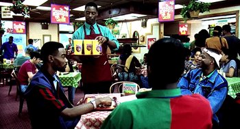 Movie still from “Clockers” (1995), directed by Spike Lee – A man in an apron is serving food to a group of people in a restaurant; Medium shot, Over the shoulder angle