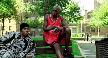 Movie still from “Clockers” (1995), directed by Spike Lee – A man sitting on top of a wooden park bench; Medium shot, Over the shoulder angle