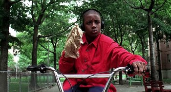 Movie still from “Clockers” (1995), directed by Spike Lee – A young man riding a bike while wearing headphones and holding a paper bag; Medium shot, Low angle
