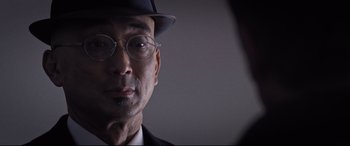 Movie still from “Death Note” (2017), directed by Adam Wingard – An older man wearing a hat and glasses; Close Up shot, Over the shoulder angle