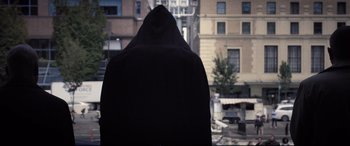 Movie still from “Death Note” (2017), directed by Adam Wingard – A person wearing a black hooded jacket in front of a building; Medium shot, Low angle