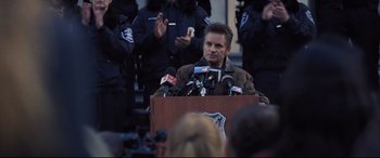 Movie still from “Death Note” (2017), directed by Adam Wingard – A man standing at a podium with microphones in front of him; Medium shot, Over the shoulder angle